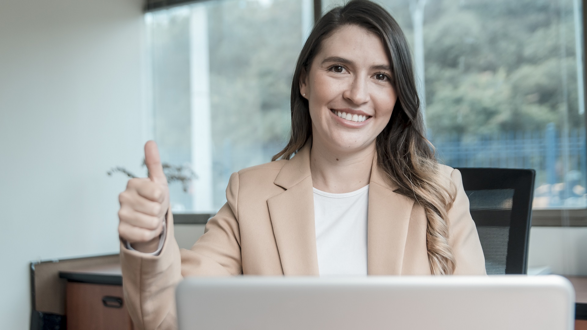 fotografía: Una jovensonriendo frente a un pc portatíl con su pulgar arriba